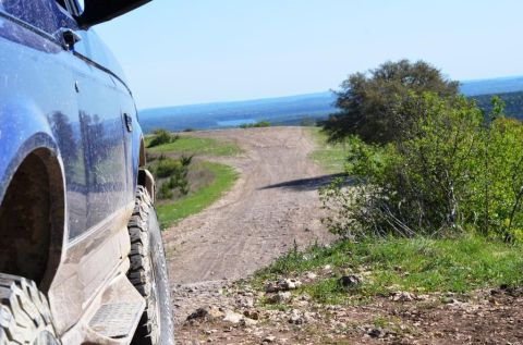 1996 Ford Bronco - A blue SUV is parked on a dirt road overlooking a scenic landscape with a lake in the distance.