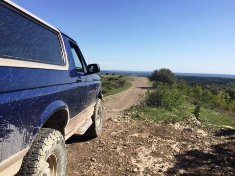 1996 Ford Bronco - A blue SUV is parked on a dirt road with a scenic view of rolling hills and a distant horizon under a clear blue sky.