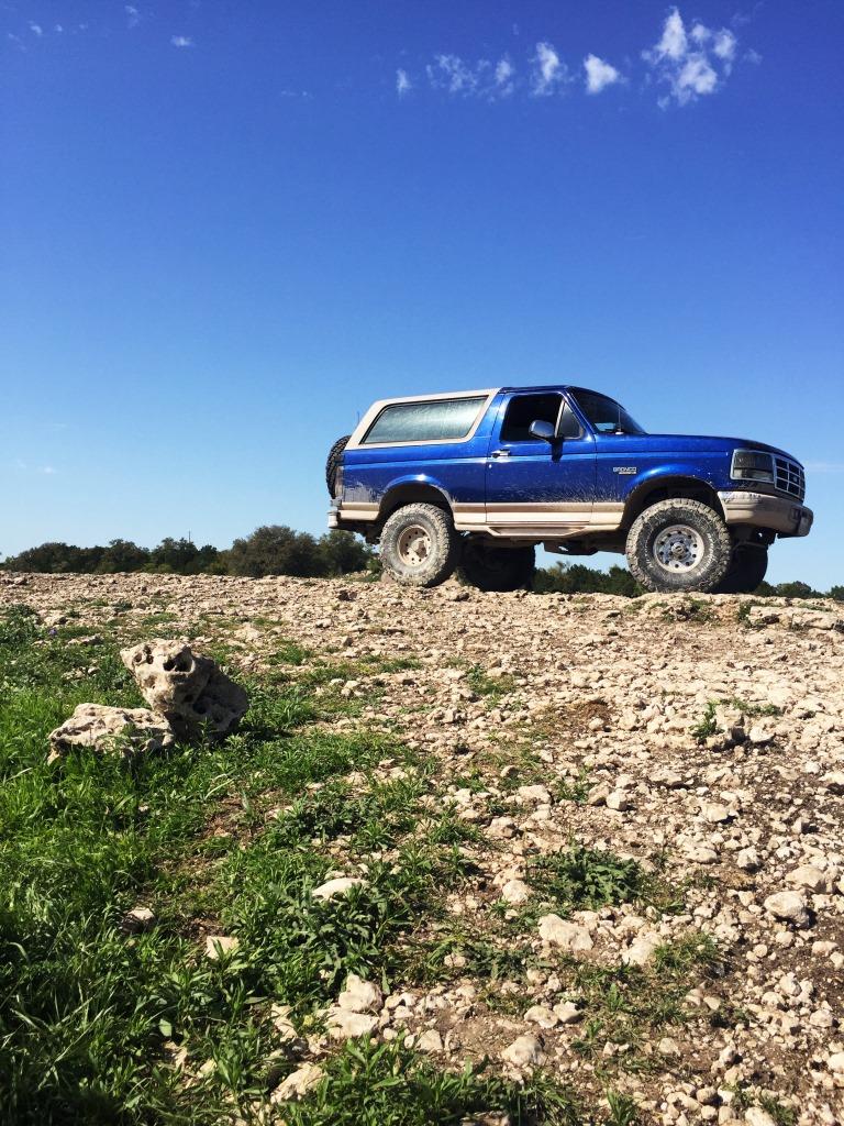 Blue 1996 Ford Bronco parked on a rocky, grassy hill under a clear blue sky