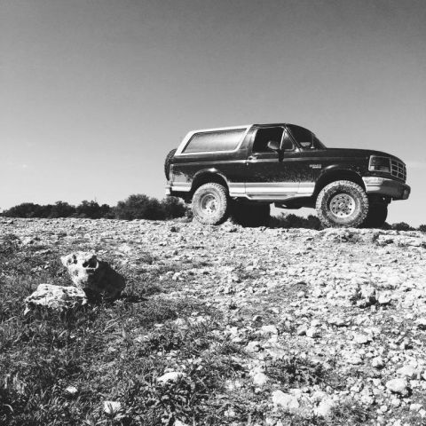 1996 Ford Bronco - A black Ford Bronco sits on a rocky incline, its spare tire mounted on the back.