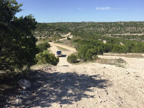 1996 Ford Bronco - A lone SUV navigates a dusty trail in a remote, arid terrain under a clear blue sky.