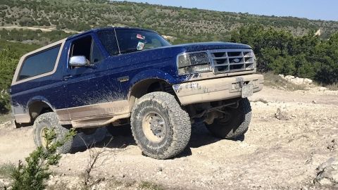 1996 Ford Bronco - 1996 Ford Bronco navigating a rough, off-road terrain with hills in the background.