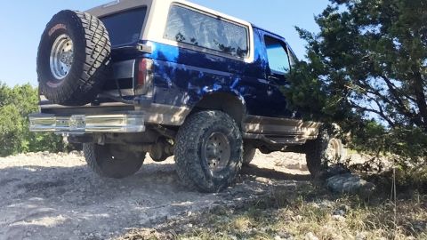 1996 Ford Bronco - This blue Ford Bronco is navigating a rough, off-road terrain.
