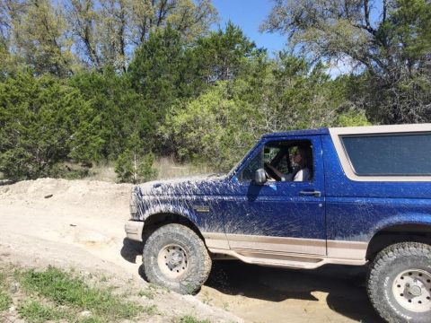 1996 Ford Bronco - Mud-splattered 1996 Ford Bronco navigates an off-road trail.