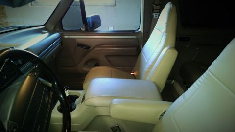 1994 Ford Bronco - The interior of a vehicle is shown, tan seats and a prominent center console with cup holders.