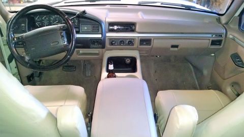 1994 Ford Bronco - The interior of a vehicle is shown, a tan dashboard and light-colored seats.