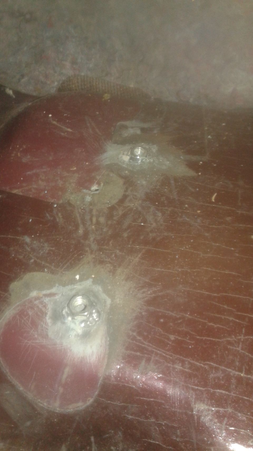 Red car body panel with two visible bolts and some damage