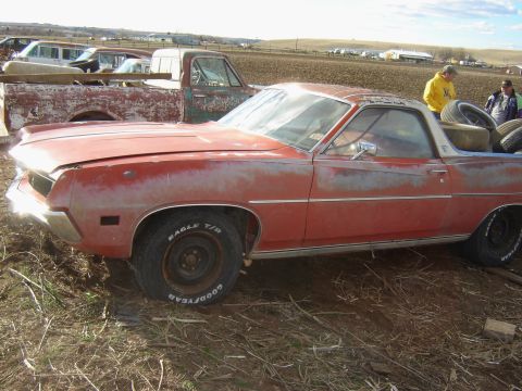 1971 Ford Ranchero - A weathered 1971 Ford Ranchero pickup truck sits in a yard with spare tires loaded in its bed.