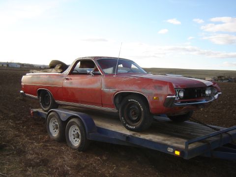 1971 Ford Ranchero - A weathered red pickup truck is being transported on a trailer across a field.