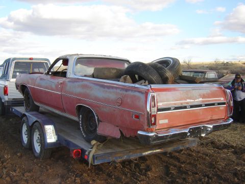 1971 Ford Ranchero - A weathered red Ford Ranchero is loaded onto a trailer, with several tires piled in its bed.