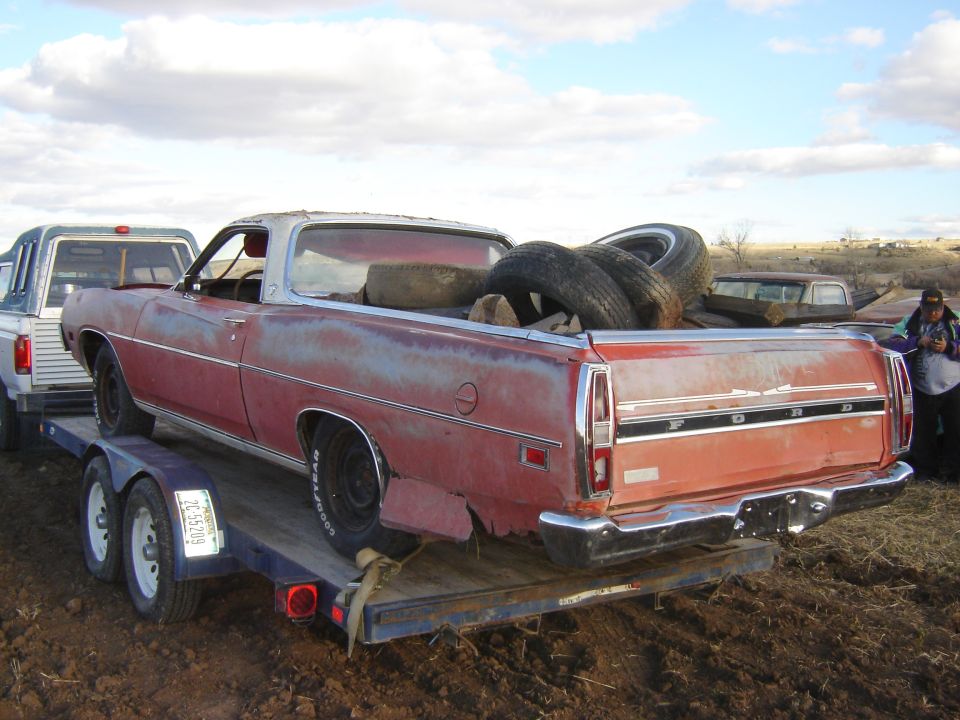 Red Ford Ranchero on trailer, carrying tires. Rust and damage visible on rear quarter panel