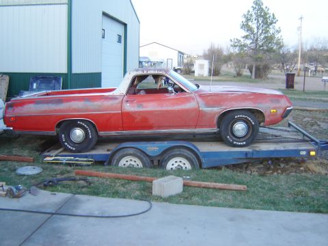 1971 Ford Ranchero - A red Ford Ranchero, likely from the early 1970s, is parked on a trailer in front of a large building.