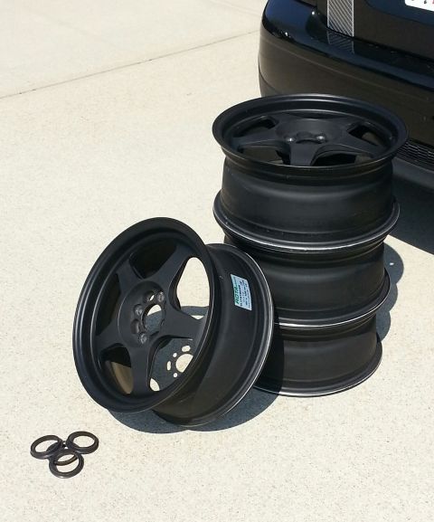 2010 MINI Cooper - Four black alloy wheels are shown, with a portion of a black vehicle in the background.
