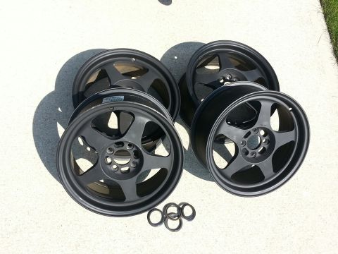 2010 MINI Cooper - A set of four dark gray alloy wheels, each a five-spoke design and a central hub, are displayed on a concrete surface.