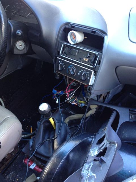 1995 Ford Probe - The dashboard of a car is shown with the radio removed and wiring exposed, an aftermarket gauge.