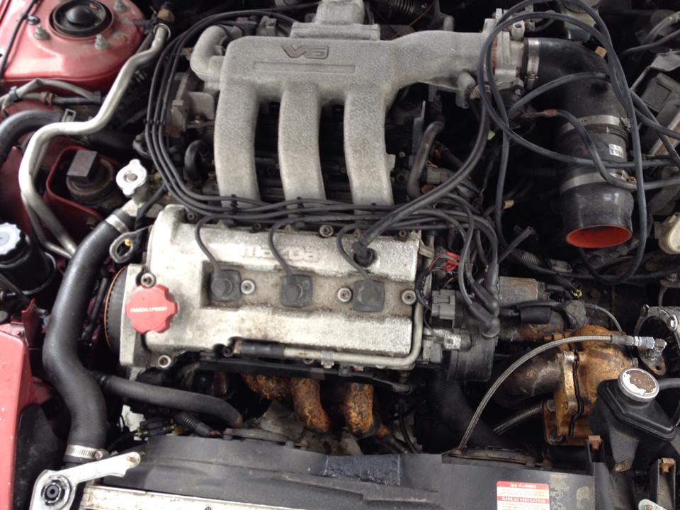 Close-up of a V6 engine bay with visible intake manifold, valve covers, and wiring.
