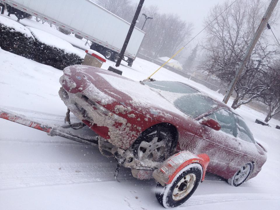 Red Ford Probe on a trailer in a snowstorm.