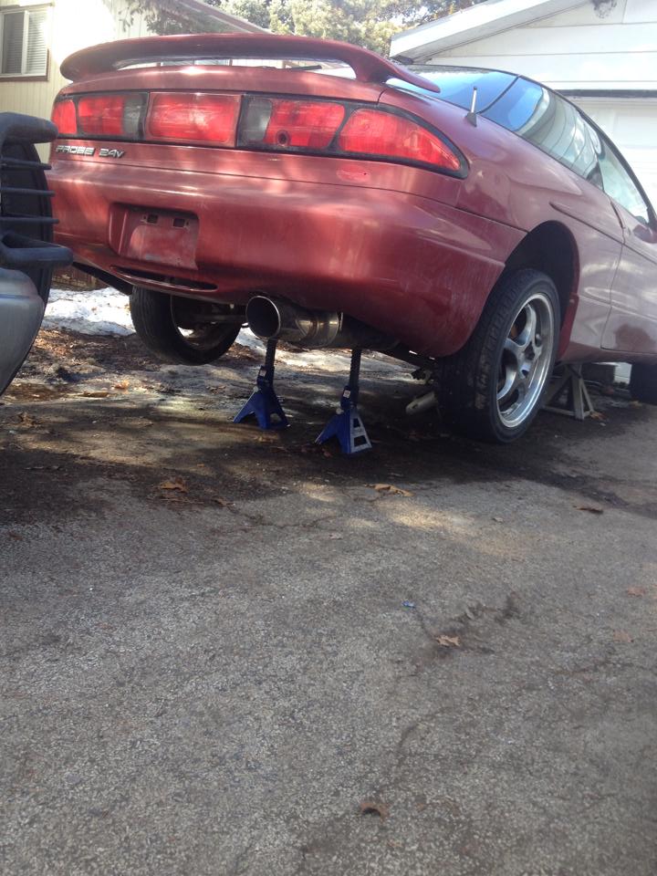Red 1995 Ford Probe on jack stands, rear view.