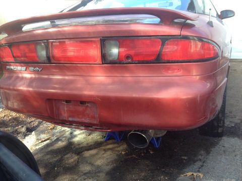 1995 Ford Probe - The rear view of a red 1995 Ford Probe GT is shown, lifted on jack stands with a visible exhaust pipe. The car has a spoiler and the 'PROBE…