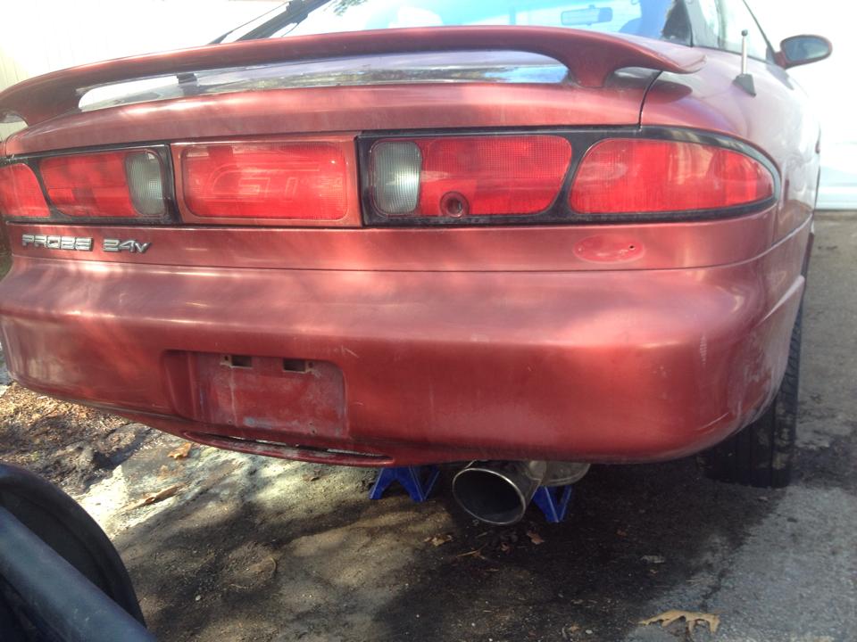 Red 1995 Ford Probe GT rear view, lifted on jack stands, with visible exhaust.