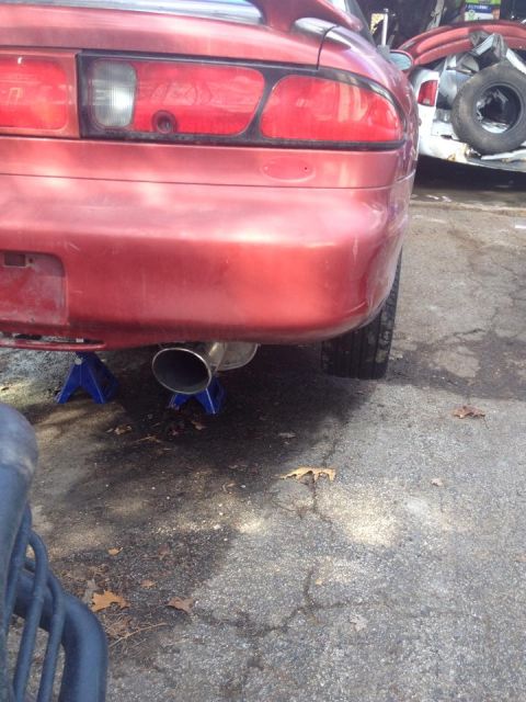 1995 Ford Probe - The rear of a red 1995 Ford Probe is shown, supported by jack stands. A large exhaust pipe is visible extending from beneath the car.