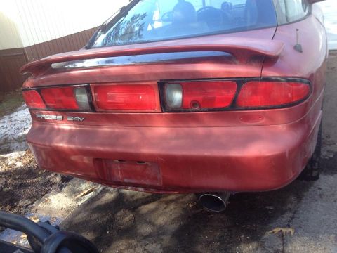 1995 Ford Probe - The rear of a red Ford Probe GT is shown, featuring its distinctive taillights and a spoiler. The "PROBE 24V" badging is visible on the tru…