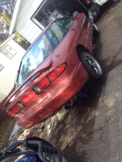 1995 Ford Probe - A red 1995 Ford Probe is parked on an asphalt driveway next to a white house and garage. The car is jacked up on a blue jack stand at the r…