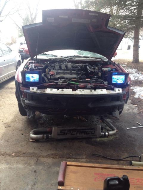 1995 Ford Probe - Front view of a red 1995 Ford Probe with the hood open, revealing the engine bay and aftermarket headlights. An intercooler is visible unde…