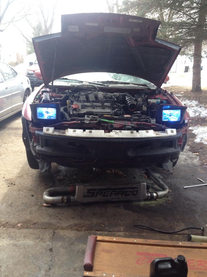Red 1995 Ford Probe with hood open, engine visible, aftermarket headlights, intercooler.