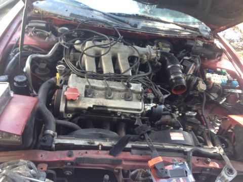 1995 Ford Probe - The engine bay of a red 1995 Ford Probe is shown, with the hood open. The V6 engine is visible, along with various hoses, wires, and the fu…