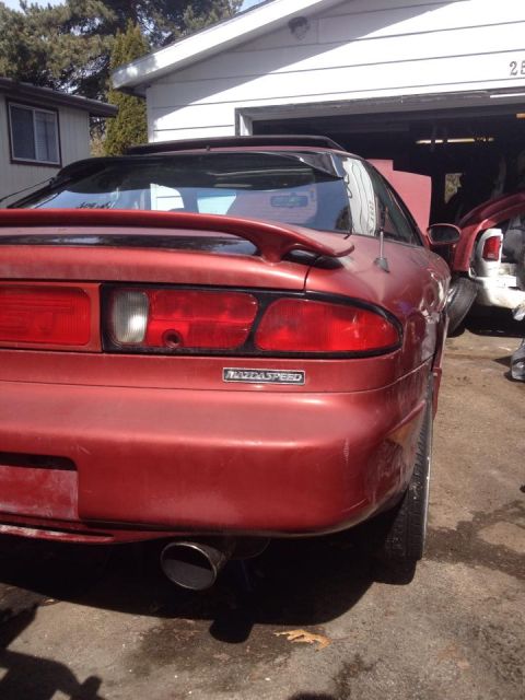 1995 Ford Probe - The rear driver's side of a red MazdaSpeed branded vehicle is shown parked in front of a garage. The car has a large spoiler and a visible…