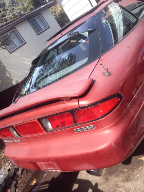 1995 Ford Probe - The rear passenger side of a red hatchback is shown in an outdoor setting, parked next to a light-colored building. Visible details include…