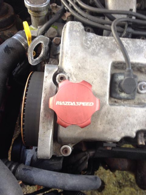 1995 Ford Probe - A close-up view of a MazdaSpeed branded red oil cap on top of a silver engine valve cover. A black timing belt is visible to the left of th…