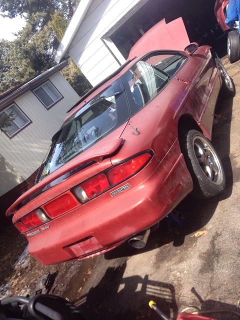 1995 Ford Probe - The rear driver's side of a red 1995 Ford Probe is shown parked in a driveway next to a garage. The car is jacked up, with the hood open an…