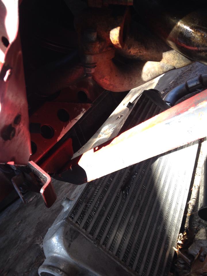 Close-up of car intercooler, red bracket, and engine parts.