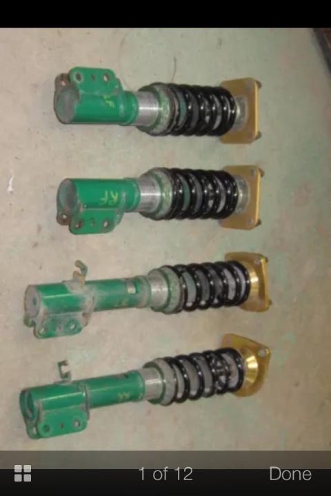 1995 Ford Probe - Four green performance coilovers with black springs are laid out horizontally on a concrete surface. Each coilover has a gold top mount and…