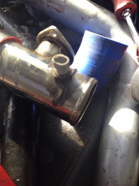 1995 Ford Probe - A close-up view of a shiny metal automotive exhaust component with a flange and a smaller outlet pipe. A blue silicone hose and other metal…