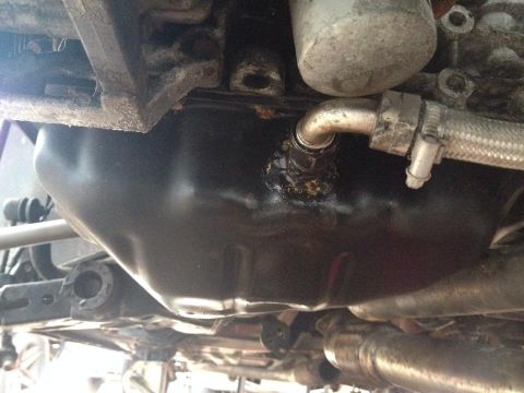 1995 Ford Probe - A close-up view of the underside of a vehicle, focusing on the engine oil pan and a braided hose connection. There is evidence of an oil le…