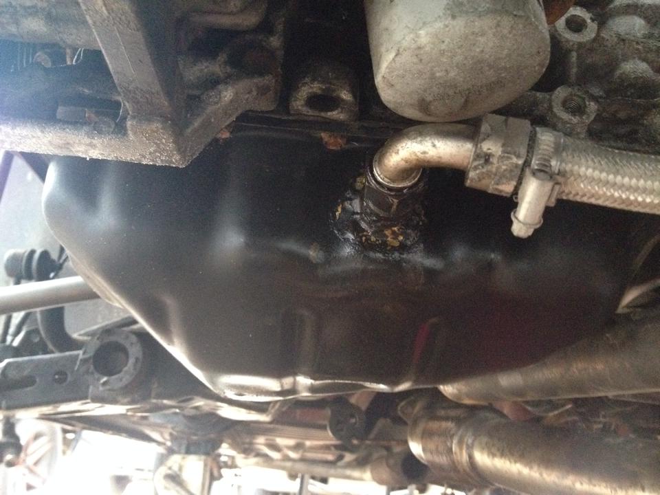 Underside of a vehicle showing an oil pan and a leaking braided hose connection.