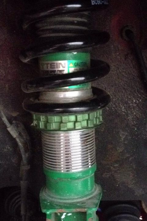 1995 Ford Probe - A close-up view of a Tein brand coilover suspension part, painted green and silver, with a black spring.