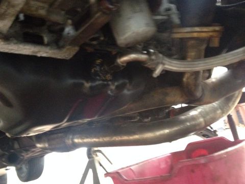 1995 Ford Probe - The underside of a vehicle, showing the oil pan, exhaust system, and part of a red oil drain pan below. The vehicle appears to be on jack s…