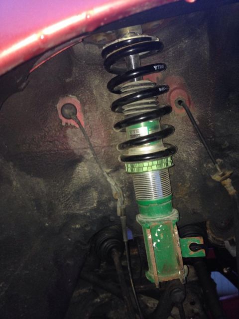 1995 Ford Probe - A close-up, low-angle shot of the front suspension of a vehicle, featuring a green adjustable coilover shock absorber with a black spring.…