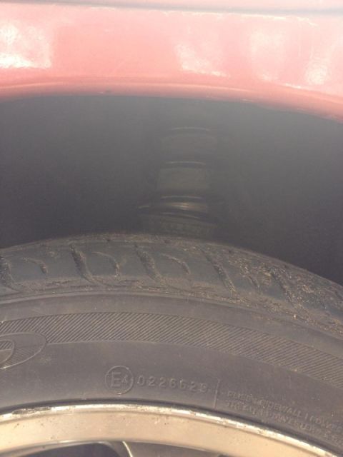 1995 Ford Probe - A close-up view of the front passenger side tire and suspension of a red vehicle. The tire has an E4 0226629 marking visible.