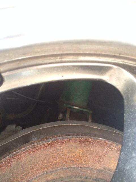 1995 Ford Probe - A close-up view of a rusty brake rotor and a green coilover suspension component is visible through the opening of a silver wheel rim.
