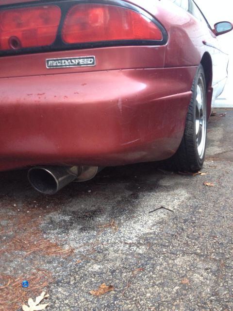 1995 Ford Probe - The rear passenger side of a red MazdaSpeed vehicle is shown, with a chrome exhaust tip visible below the bumper. The car is parked on a we…