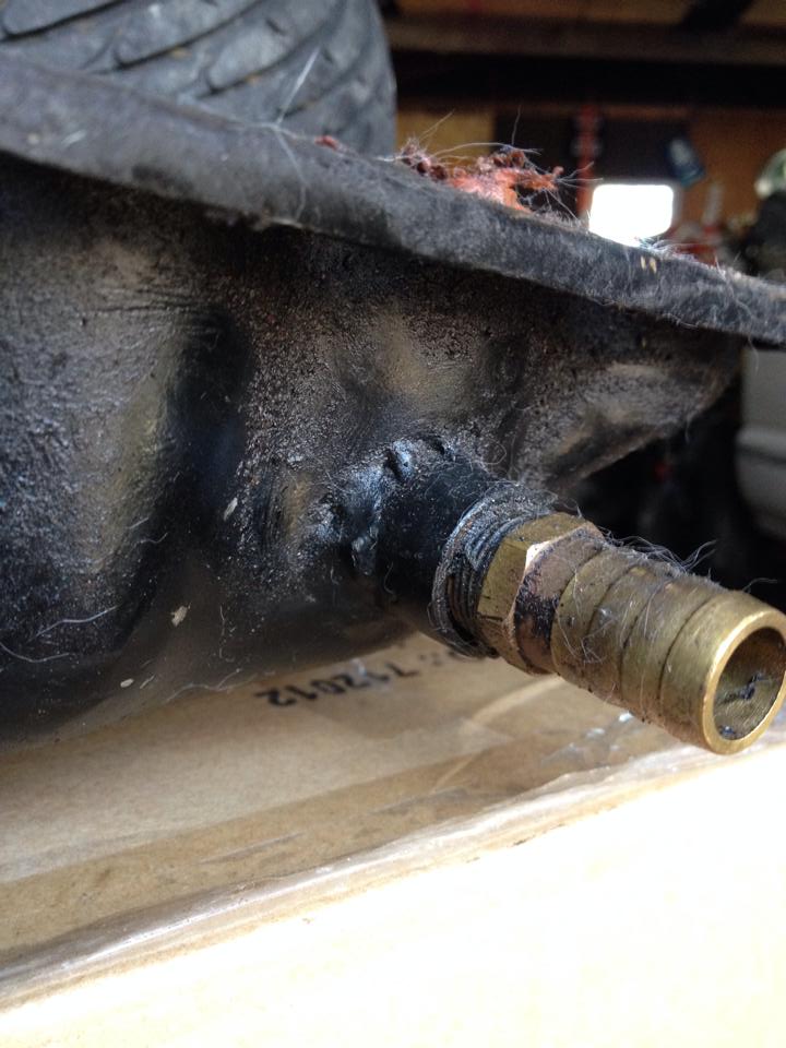 Close-up of black textured part with brass fitting and hose, text "112012" visible.