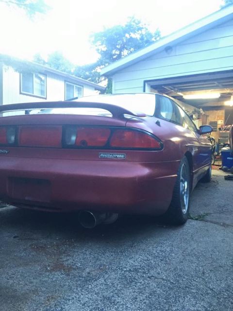 1995 Ford Probe - The rear driver's side quarter view of a red 1995 Ford Probe is shown parked in a driveway next to a garage. The car features a spoiler and…