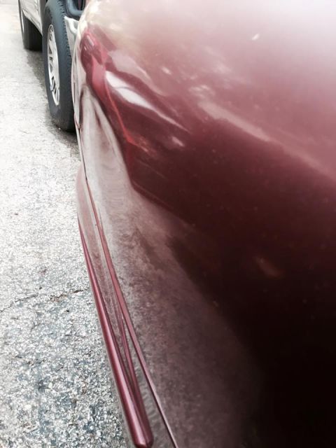 1995 Ford Probe - A close-up of a dented side panel on a dark red vehicle parked next to a silver SUV.