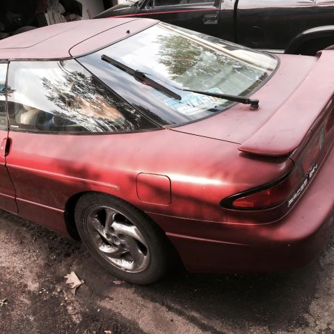 1995 Ford Probe - The rear passenger side of a red 1995 Ford Probe is shown. A black pickup truck is parked behind it.