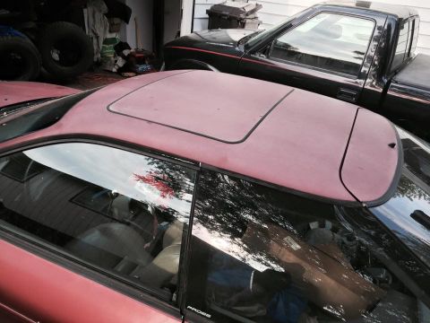 1995 Ford Probe - The dusty, maroon sunroof panel and surrounding trim of a coupe are visible, with a black pickup truck parked behind it. The side window re…